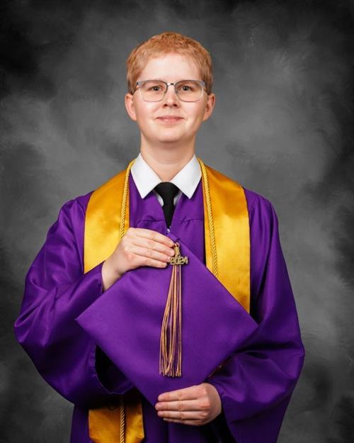 A teenage boy in a purple graduation gown holding a cap with a gold still